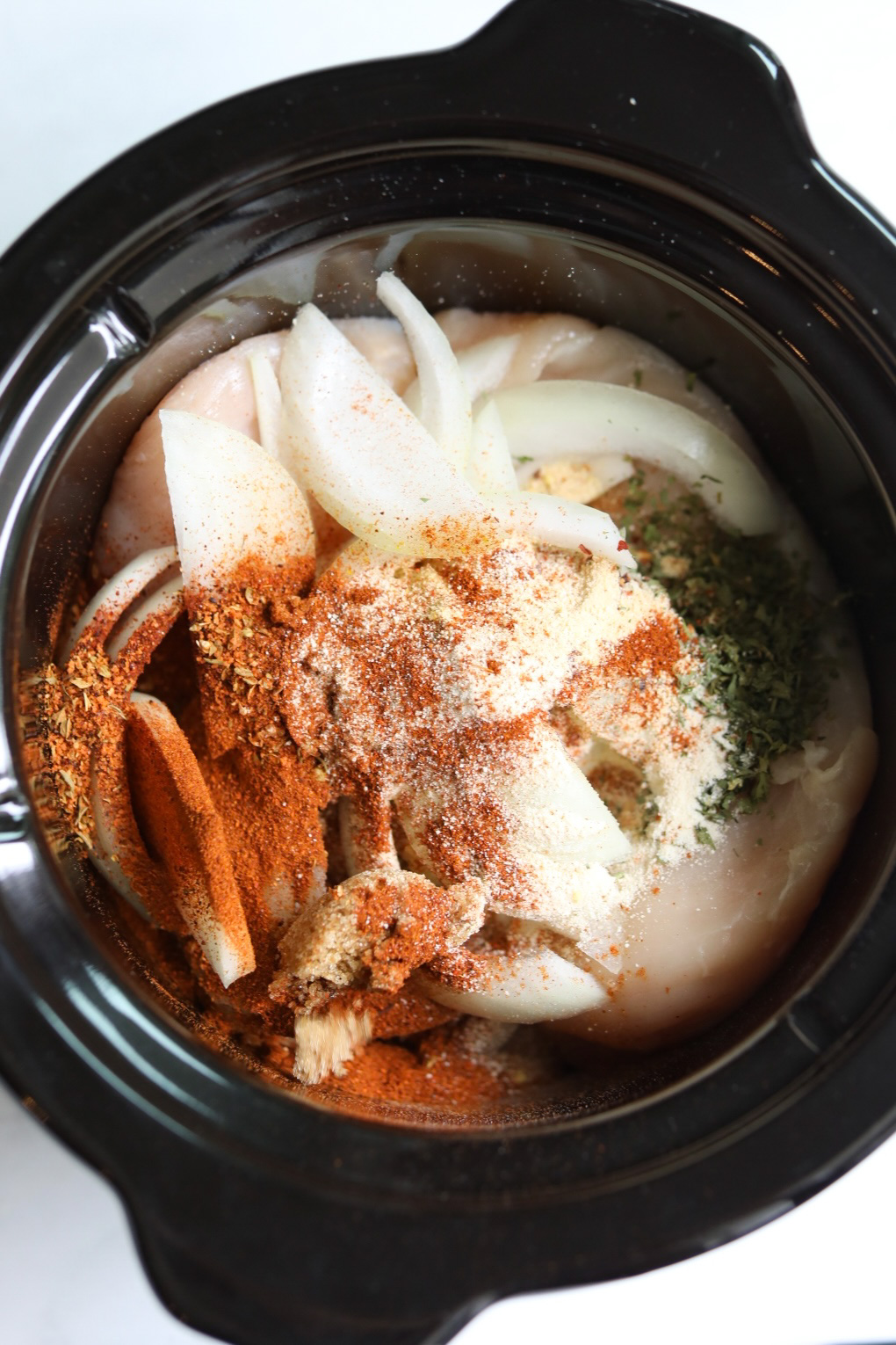 onions and spice blend added to a crockpot filled with chicken breasts