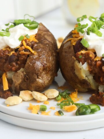 Featured image for baked potato with chili, topped with cheddar cheese, sour cream, chives, jalapeño and cilantro. For styling purposes, oyster crackers and cilantro added for styling purposes.