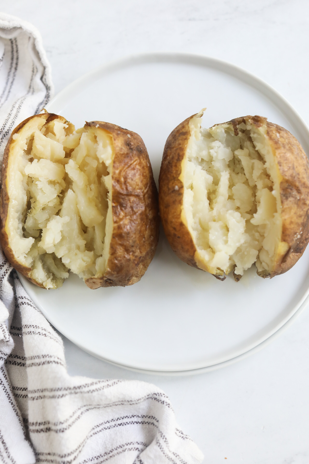 Plain baked potato sliced open and contents of potato fluffed with a fork before stuffing potatoes with chili.