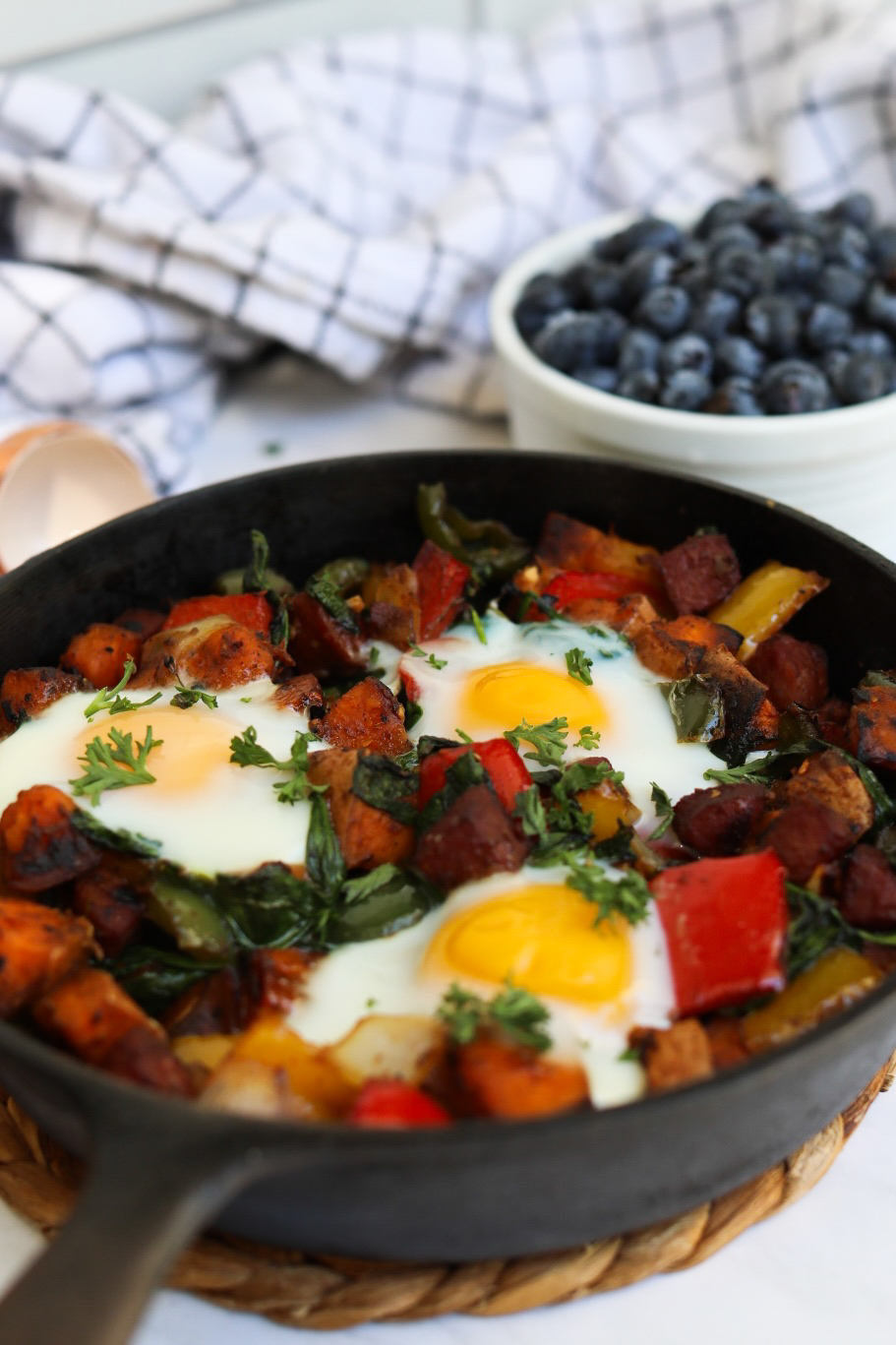 Final recipe plated in a small black cast iron skillet with three runny eggs on top of sweet potato hash.