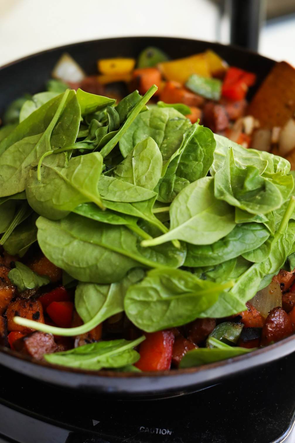 Potato hash cooked through and adding fresh spinach in the final stages of recipe.