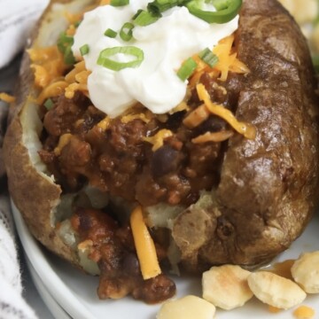 Zoomed in image of chili baked potato and toppings. Oyster crackers and black and white kitchen towel added for styling purposes.