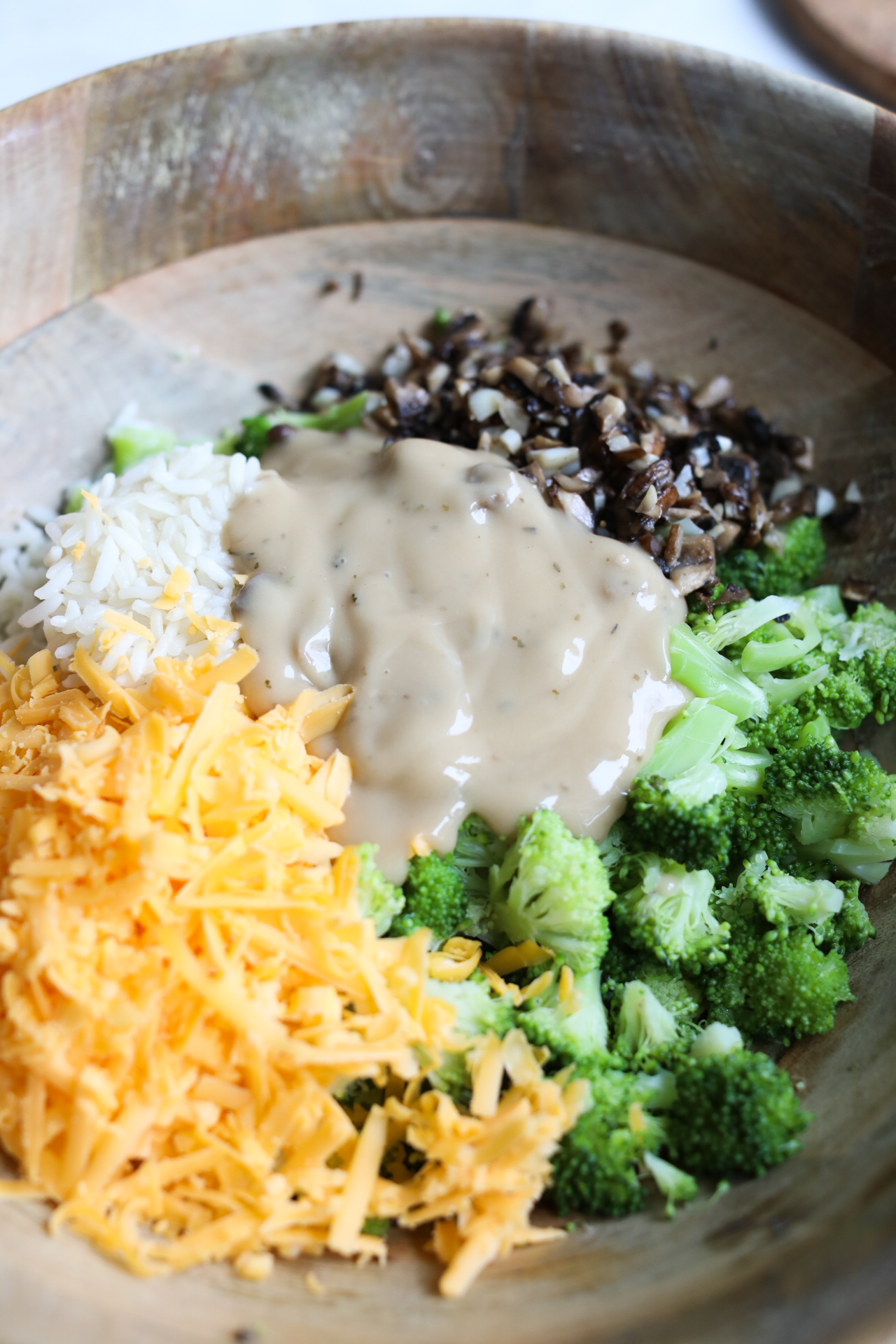 Process shot of casserole recipe in wooden bowl; broccoli, cheddar, rice, mushrooms, garlic and mushroom soup.