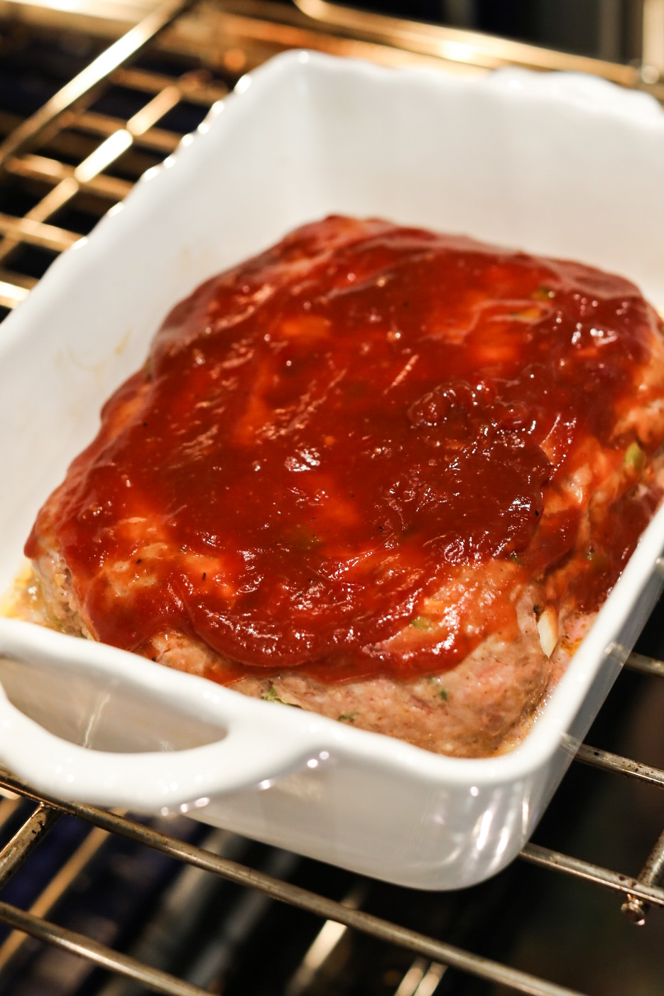 Recipe with meatloaf and sauce in baking dish in the oven.