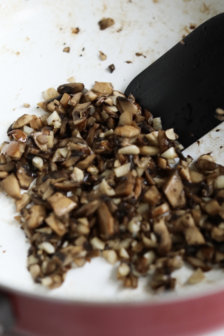 Sautéed mushroom and garlic in pot with black spatula.