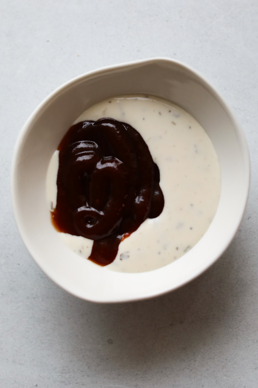 BBQ Ranch ingredients in a small white bowl. Ranch and BBQ sauce are in the bowl un-mixed.