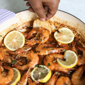 Hand scooping BBQ Shrimp with crusty bread.