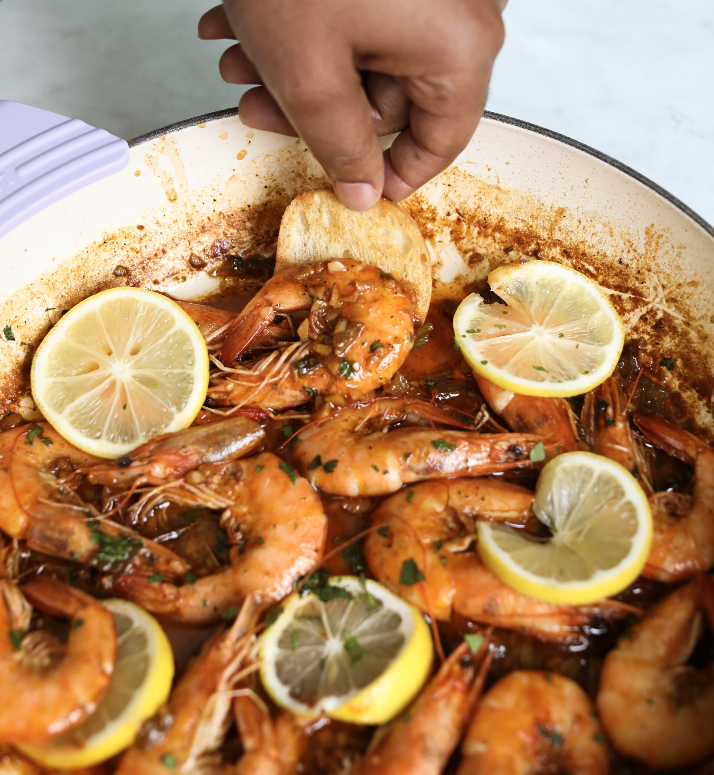 a hand dipping a piece of bread into a pot containing New Orleans style bbq shrimp