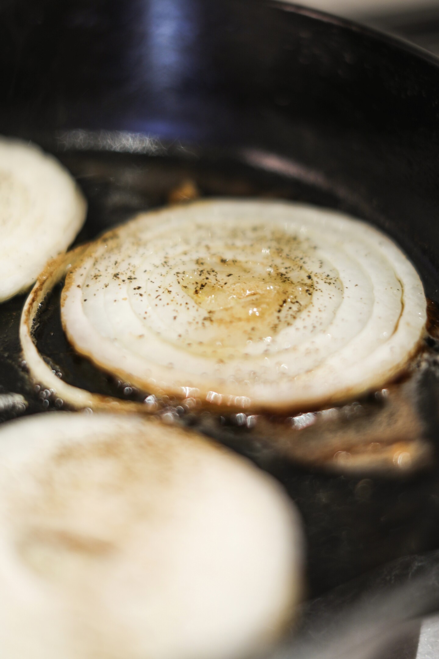 Grilled onion rounds par cooked in black cast iron skillet.