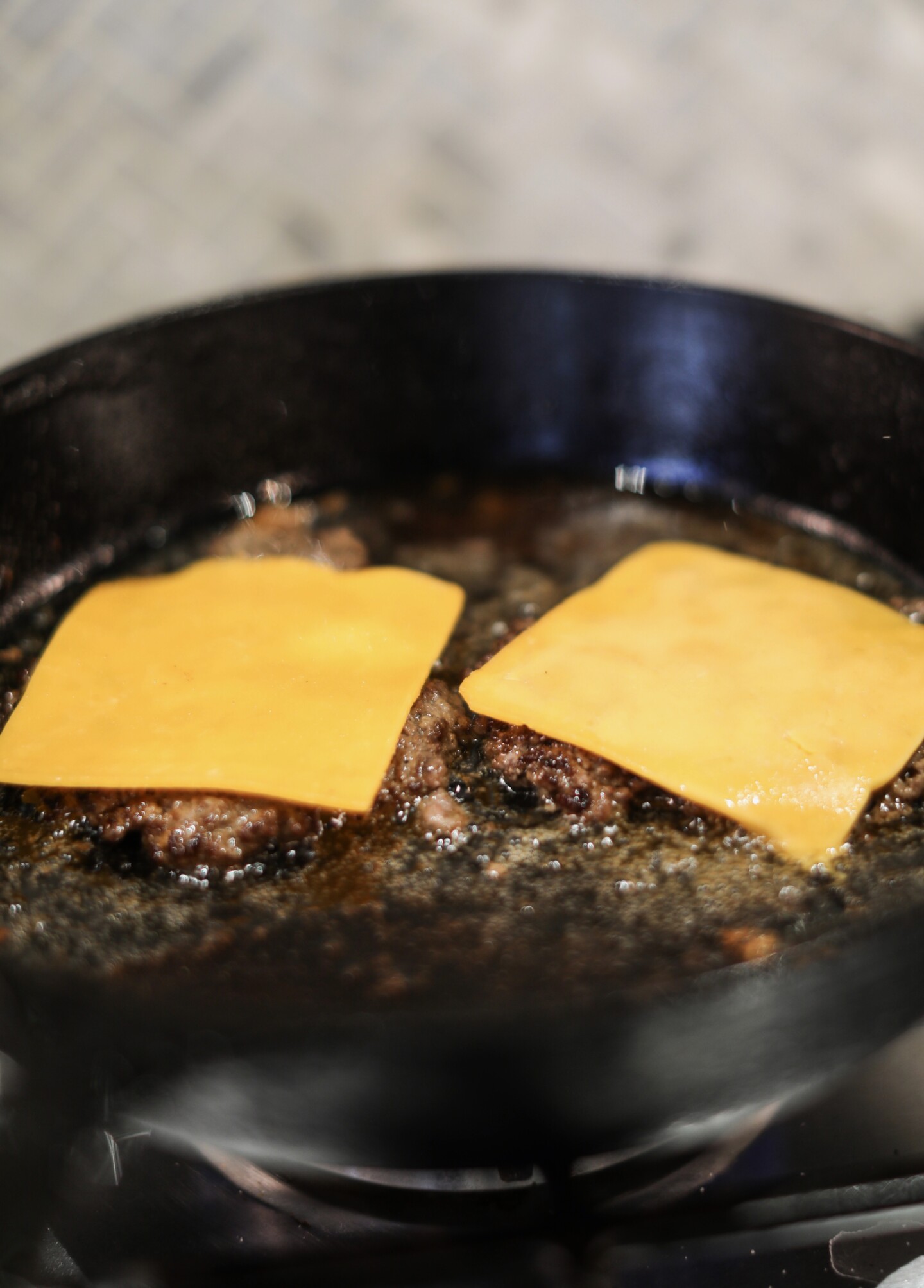 Process shot of burger patties grilled in a cast iron skillet.