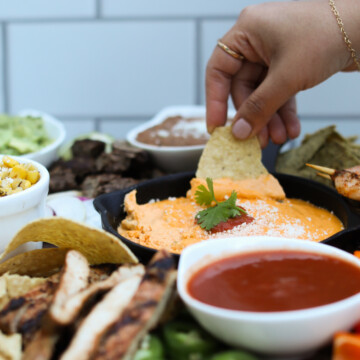 Nacho board final recipe with hand dipping with chip in cheese.