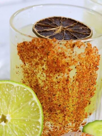 Featured image of cucumber margarita, dressed with a rimmed tajin rim with sliced lime and cucumber.