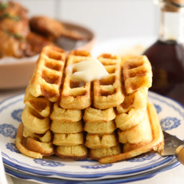 Completed recipe of cornbread waffles plated and piled high with a slice of melting butter on top.
