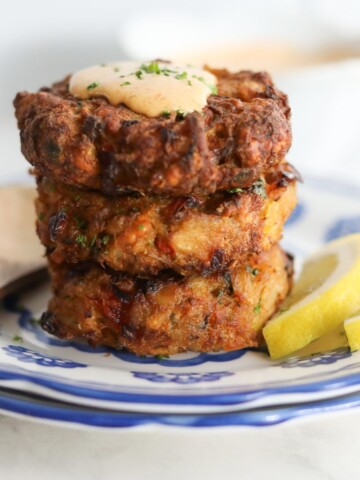 Final image of air fryer crab cakes stacked on a blue and white plate with remoulade sauce on top.