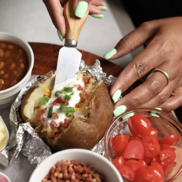 Hand dipping sour cream in baked potato on designed baked potato bar.