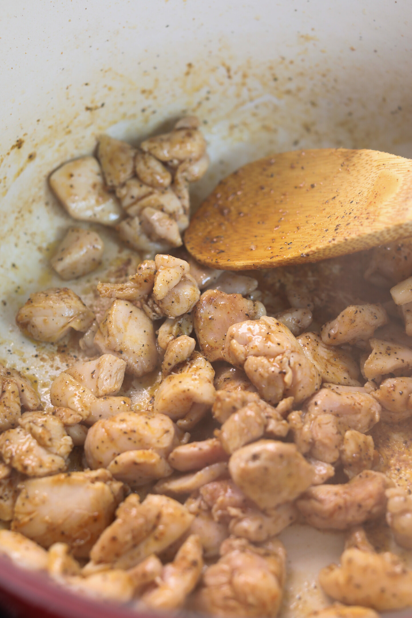 Chicken thighs sautéing in dutch oven with cajun seasoning and wooden spoon.