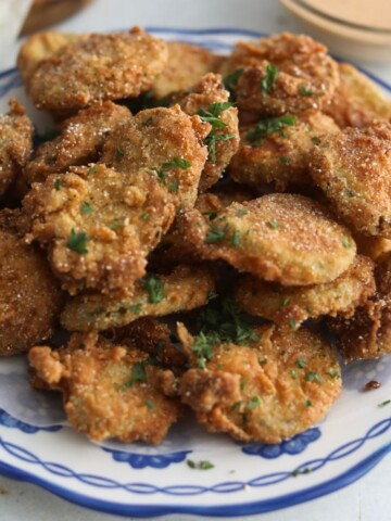 Fried pickles plated on blue and white plate with parsley and remoulade sauce.