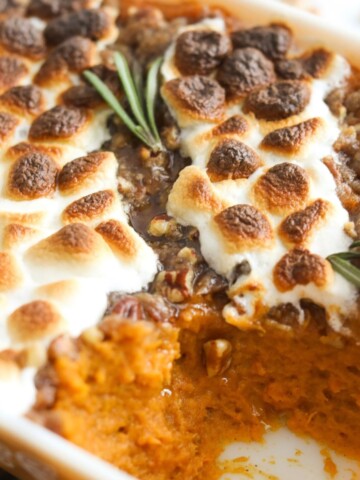 Sweet potato casserole with pecans topped with golden marshmallows and garnished with fresh rosemary.