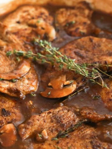 Smothered turkey chops simmering in mushroom gravy with fresh thyme sprigs.