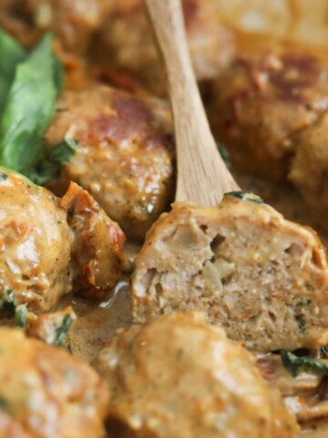 Juicy turkey meatball cut open to show the tender inside, sitting in creamy Tuscan sauce with spinach.