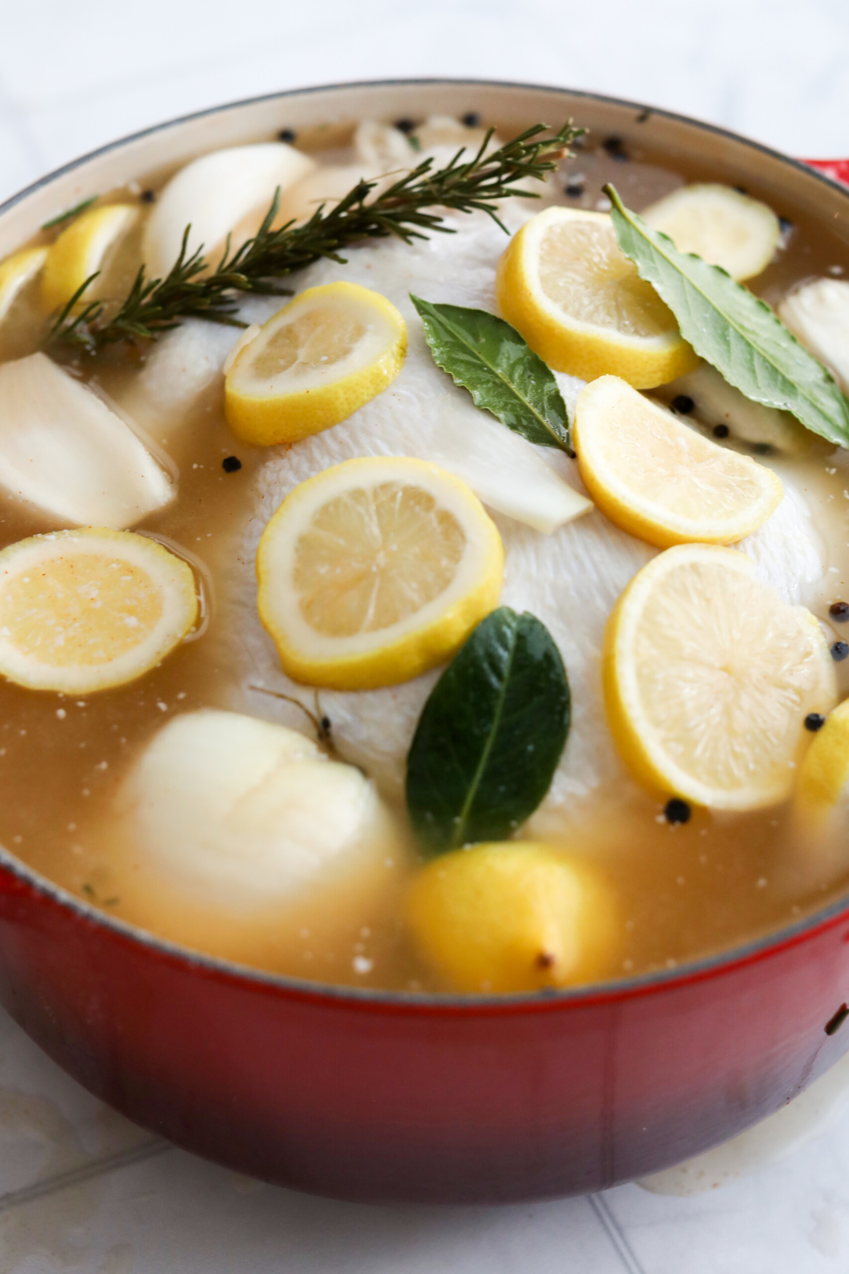 how to brine chicken A pot of chicken brine with lemon slices, rosemary, bay leaves, and black peppercorns visible on top.
