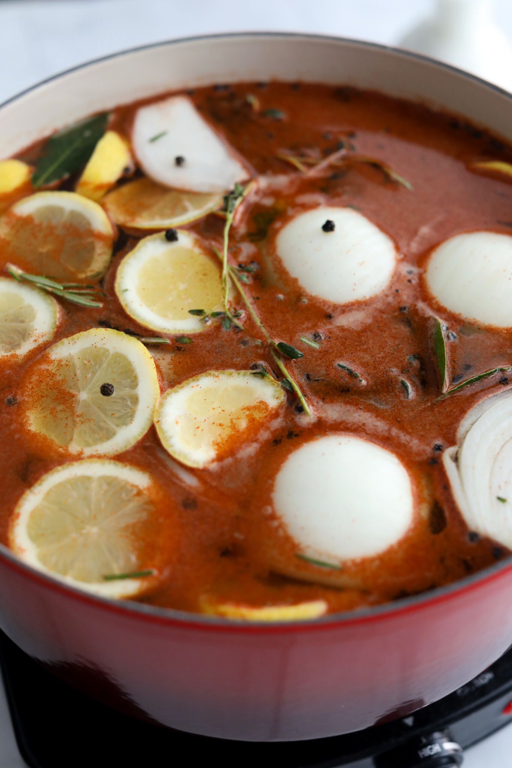 A side view of a red pot with a whole chicken soaking in lemon and herb brine.