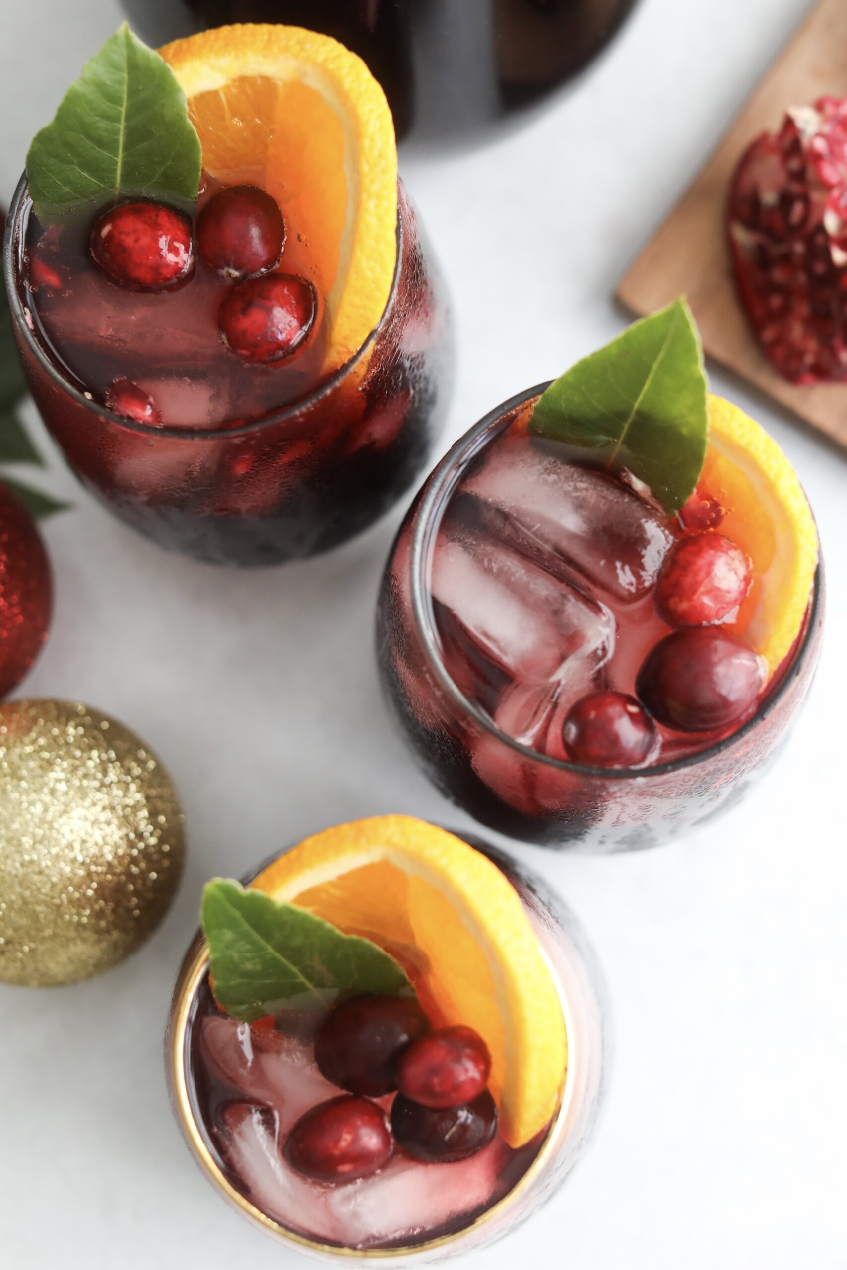 How to make Christmas punch Three glasses of Christmas Punch on ice, each topped with cranberries, orange slices, and fresh green leaves for a festive look.