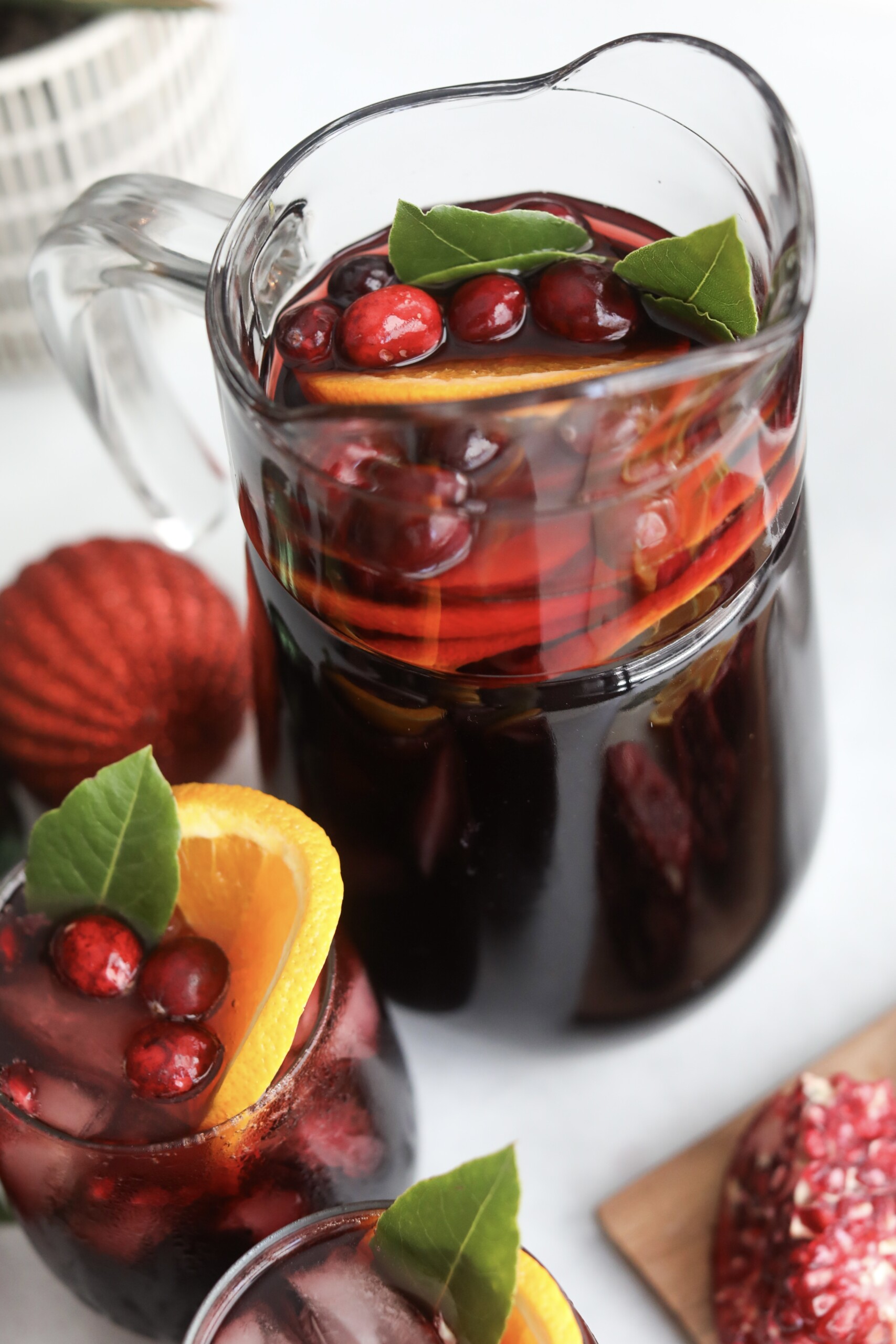Christmas punch drink Large glass pitcher of red Christmas Punch surrounded by filled glasses, decorated with orange slices, cranberries, and greenery.