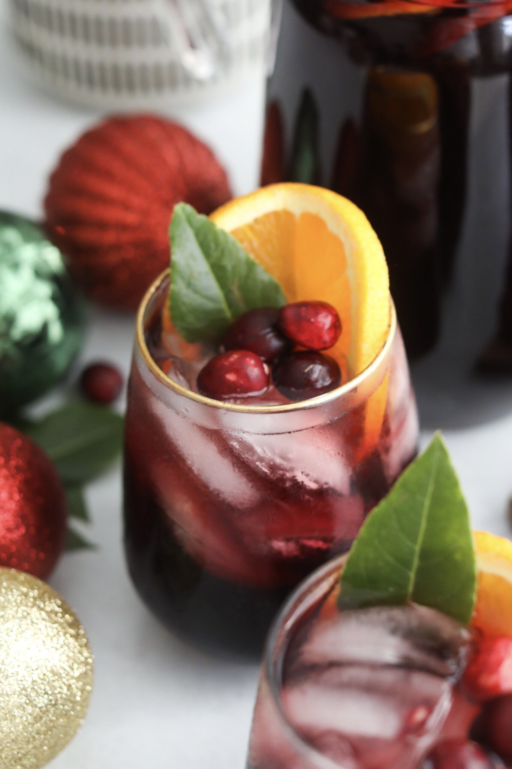 Christmas punch alcoholic Single glass of Christmas Punch with ice, garnished with an orange slice, cranberries, and a green leaf, surrounded by colorful ornaments.
